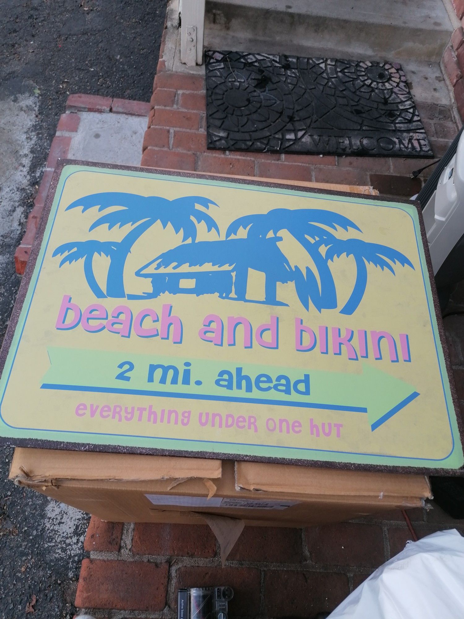 Metal sign says Beach and Bekini 2. Mi ahead every thing under one hut