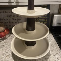 three-tiered serving tray with cream-colored plates* and dark brown wooden center columns…. bottom…* see second photo the bottom tier had a crack that