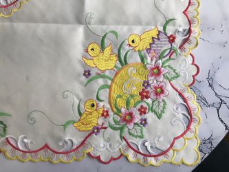 This is an embroidered table topper featuring colorful floral and chick designs with scalloped edges. 34”