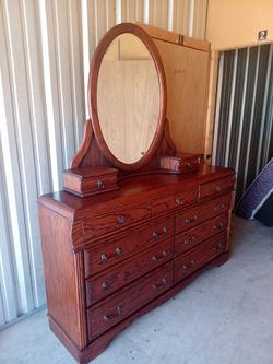 Elegant wooden dresser with an oval mirror and multiple drawers.