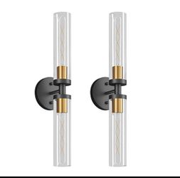 Elegant wall sconces with clear glass cylindrical shades and a dual-tone black and gold metal finish. Each fixture has a circular black wall mount and