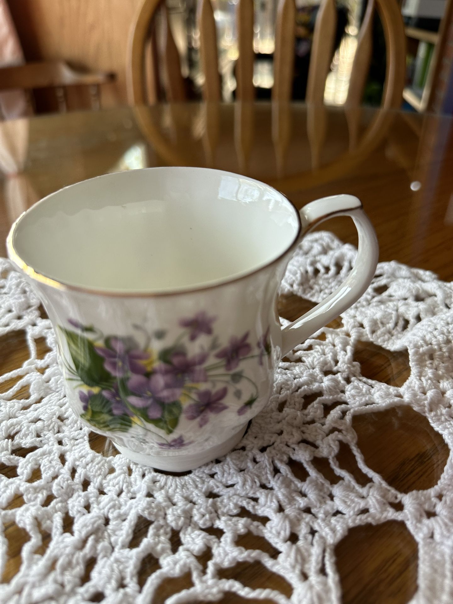 China coffee cup featuring a beautiful white design with gold trim and vibrant purple flowers.