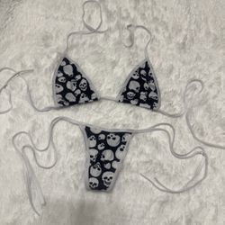 Two-piece string bikini with black fabric and white skull print. White trim and adjustable tie straps. Bold, edgy graphic look. Lightweight swim or be