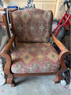Sturdy wooden armchair has tapestry upholstery with red and gold geometric patterns. Frame is solid wood with curved armrests and decorative feet.