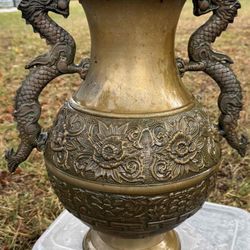 A vintage brass vase with dragon handles and embossed floral motifs.