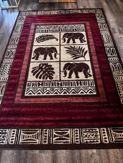 Brand new condition Burgundy rectangular area rug has central panel with elephant and tropical leaf motifs. Border features cream and black tribal geo