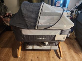 Versatile TouHeart bedside bassinet is grey with a breathable mesh design and wooden-style legs.