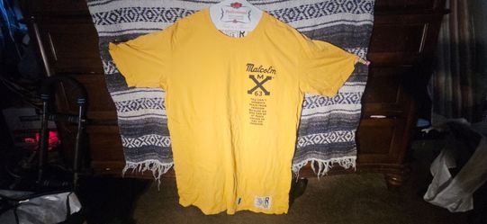 Yellow short-sleeve T-shirt featuring a bold Malcolm X 63 graphic with the quote, “You can’t separate peace from freedom because no one can be at peac