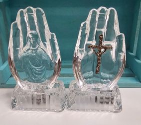 crystal glass sculptures shaped like praying hands on bases, with an embossed depiction of the Virgin Mary on the left and a metal crucifix inset on t