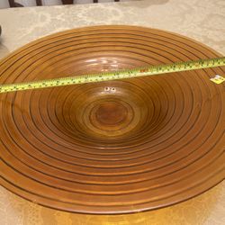 This image features a large, ribbed amber glass bowl, likely a vintage or antique piece, as suggested by its design and material. The measuring tape i