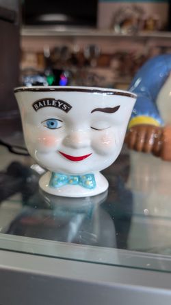 Vintage Baileys ceramic winking face novelty egg cup featuring playful molded facial details and Baileys branding. Fun MCM-style promotional barware c