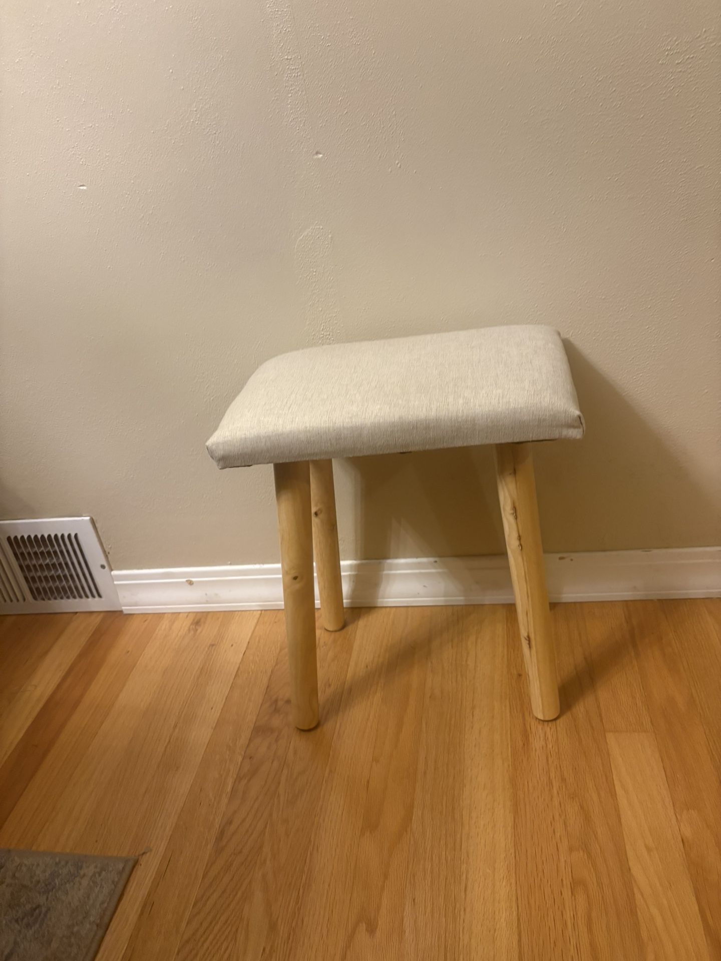 small vanity stool with solid wood legs and a light-colored, upholstered cushion