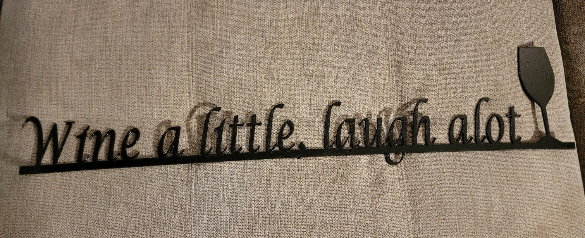Black Elizabeth Keith metal wall sign with the phrase "Wine a little, laugh alot" and a wine glass shape. 29" L x 6" W