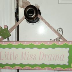 13"x5" Wooden "Little Miss Drama" Sign That Includes a Crown on a Spring, clear beads on a curled wire, and an opaque pink ribbon for hanging