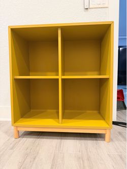 IKEA Eket storage shelf 4x4 in mustard yellow on elevated wooden base with legs
