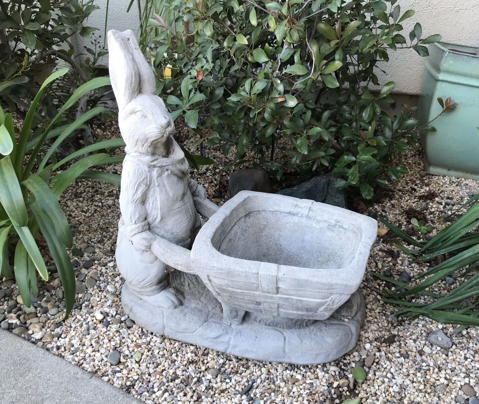 An adorable cement rabbit pushing cart planter