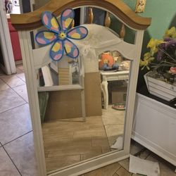 white wooden dresser mirror with a light wood top and an attached flower pinwheel decoration. 
