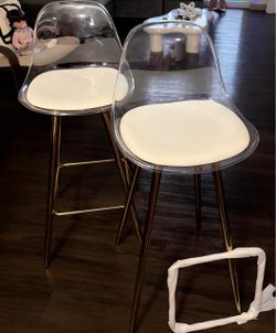 Juego de 2 sillas altas transparentes con patas doradas.