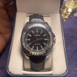 Anne Klein women's watch with a black dial, rhinestone-set bezel, and black leather band.
