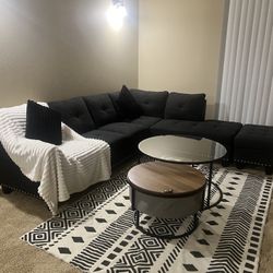 A black couch, an ottoman chair, and two tables.