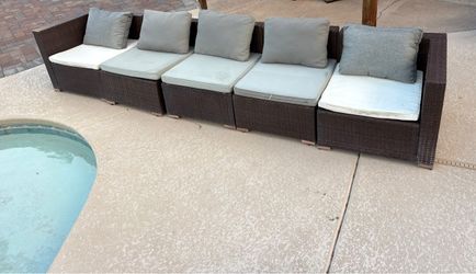 5 pcs modular brown wicker outdoor patio sofa featuring plush light-colored seat cushions and grey back pillows arranged alongside a pool.