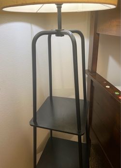 modern black floor lamp features a functional two-tier display shelf and a white linen drum shade