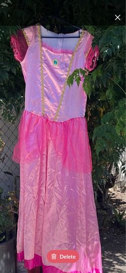 vestido es un disfraz de princesa rosa estilo "Princess Peach" con adornos dorados y mangas de tul abullonadas.