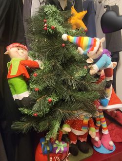 plush, poseable elf Christmas decorations with long, dangling legs, as well as an artificial mini Christmas tree that the elves are displayed on. The 