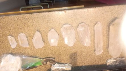 eight natural clear quartz crystal points arranged by size on a speckled surface.