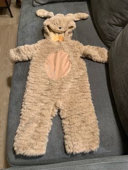 Plush tan animal costume onesie has a hooded design with long floppy ears and a peach-colored belly patch. This one-piece suit is made of fuzzy faux f