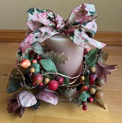 Floral arrangement with wood fruit and bow set around a wax candle sitting on a glass plate.