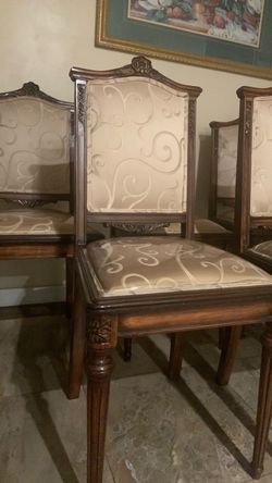 Louis XVI style carved wood dining chairs feature a rich mahogany finish and patterned beige damask upholstery on both the backrest and seat.