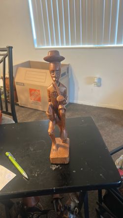 This object is a vintage, hand-carved Afro-Caribbean folk art wooden figurine depicting a man smoking a pipe