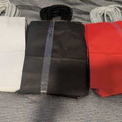 Set of 75 three stacks of plain paper shopping bags with twisted handles in white, black, and red.