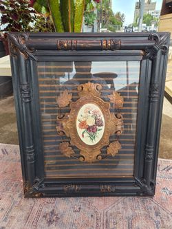 This vintage-style decorative picture features an ornate black frame and a central floral motif in copper and colorful tones.