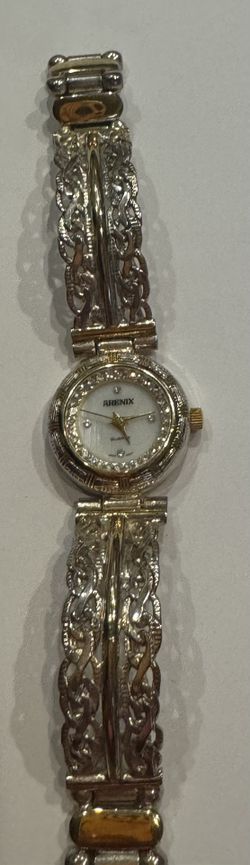 These are women's quartz watches from the Arenix brand in a vintage style. The watch features a two-tone metal bracelet and an oval dial with crystals