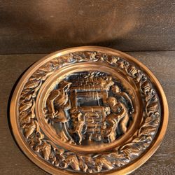 This is a vintage copper wall plate, often referred to as "Family at the Well" or "Family at the Well