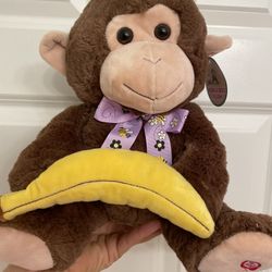 Hug fun peek a boo 11.5" tall monkey,  brown & beige with a purple floral bumblebee ribbon at neck holding a banana. Press the foot and it lifts the b
