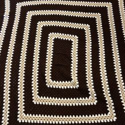 This item is a handmade crocheted throw blanket featuring a geometric pattern in brown, beige, and cream colors
