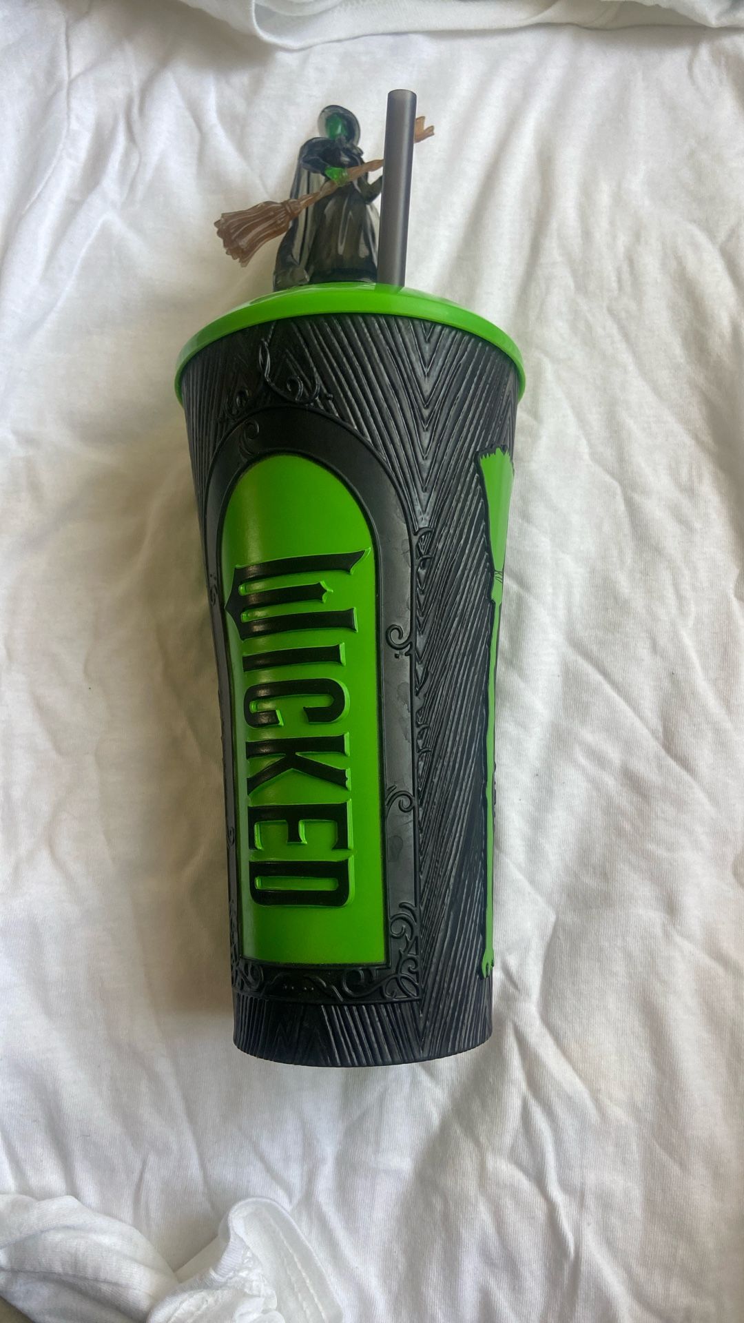 The AMC Wicked Elphaba Grippr Cup & Topper with Straw inspired by the movie "Wicked." This product is perfect for fans of the film looking to add a to