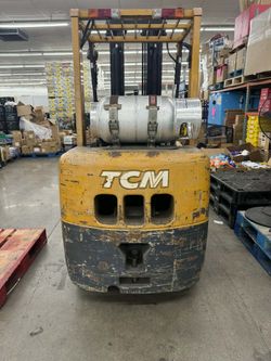 Propane-powered TCM FCG25F9 forklift has a yellow and dark grey metal body. This industrial vehicle is equipped with a rear-mounted propane tank, a p