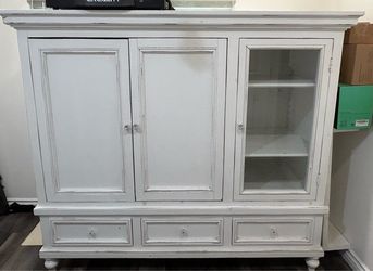 White entertainment hutch with three bottom drawers and side cabinet with glass door