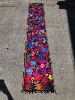 Handcrafted Mexican table runner in black fabric with vibrant, multicolored floral embroidery.