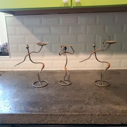 Three candle holder figures made out of metal.