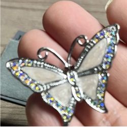 Elegant butterfly pendant with white enamel wings and iridescent crystal accents. Shiny silver-tone metal frame highlights the delicate design. Adds a