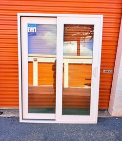 New sliding glass patio doors 60x80 in Impact Rated Galss. One door has a white frame, the other has a dark brown frame. Each door has two clear glass