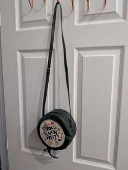 Round Crossbody Bag with 'Strong is the New Pretty' EmbroideryStylish round crossbody bag is dark green faux leather with an adjustable shoulder strap