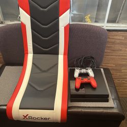 Sony PlayStation 4 console, likely the Slim model, along with two DualShock 4 wireless controllers, one red and one silver. 