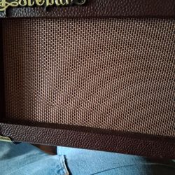 It is a 12-watt solid-state amplifier designed for practicing. 
The amplifier features a portable design with a leather-like handle and brown finish. 