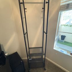 Black metal clothing rack with shelves, hooks, and wheels